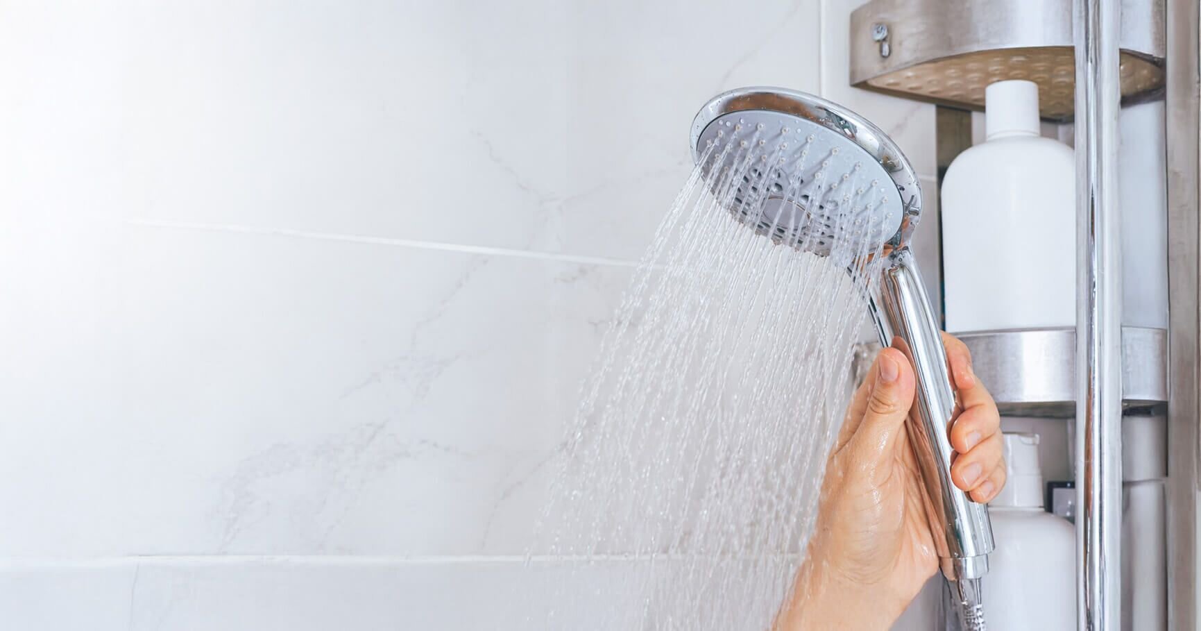A shower running in a home bathroom, with the water softener and tank visible behind it
