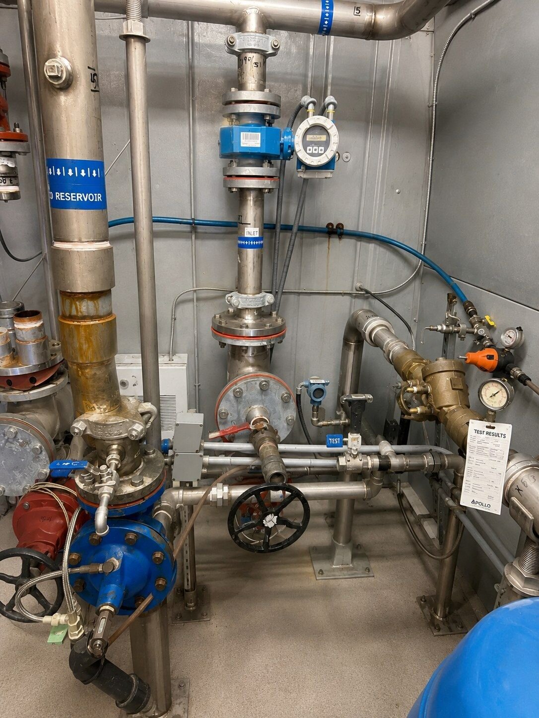 A brass backflow preventer in a plant room carrying a completed test results tag